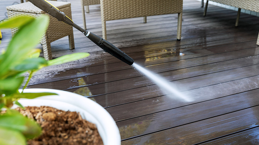 A closeup of pressure washing equipment cleaning a wooden deck